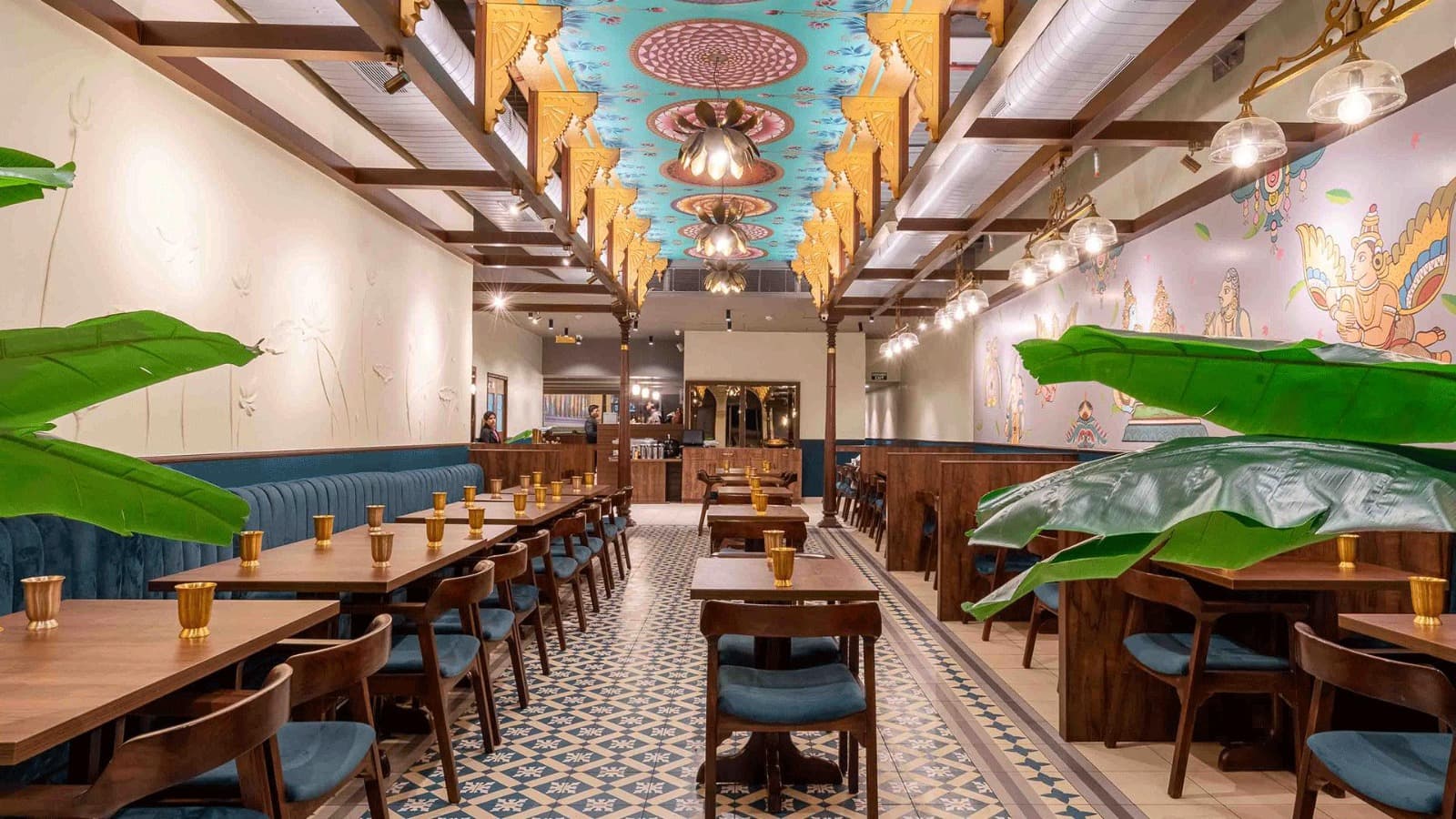 Ornate Indian restaurant with a teal lotus ceiling, patterned tile floors, and wooden dining tables.