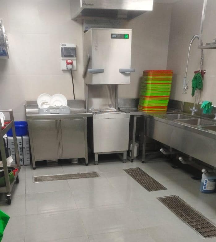 Commercial kitchen dishwashing station with stainless steel pass-through dishwasher, large sink, and trays.