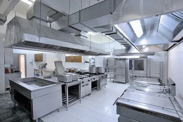 Modern commercial kitchen featuring stainless steel appliances, large ventilation hoods, and white tile floors.