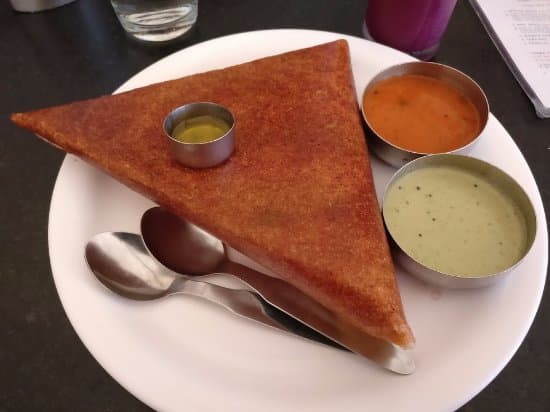 Crispy triangular dosa on a white plate with three small bowls of colorful chutneys.